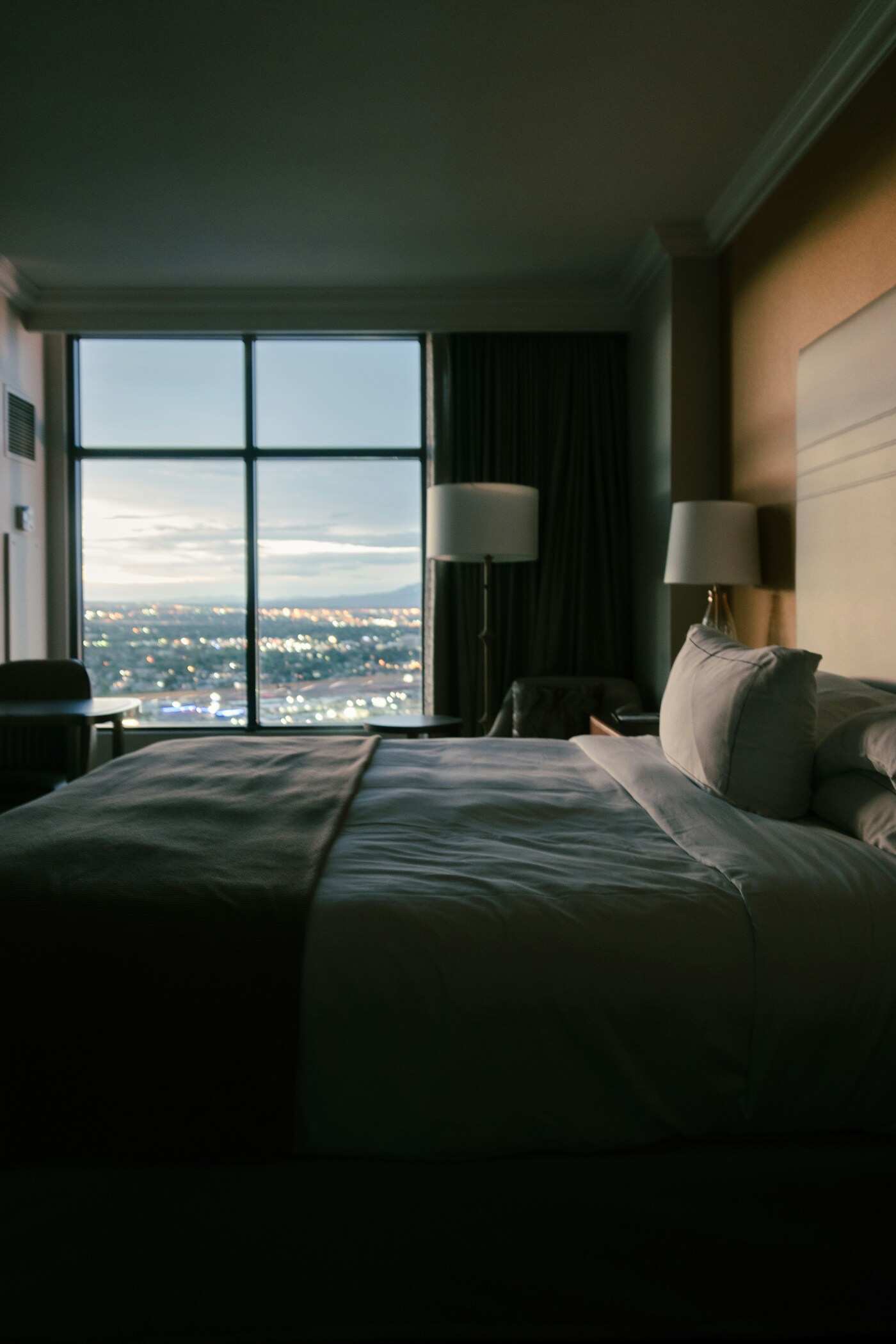 A double bed facing a floor-to-ceiling window, the city below at dusk