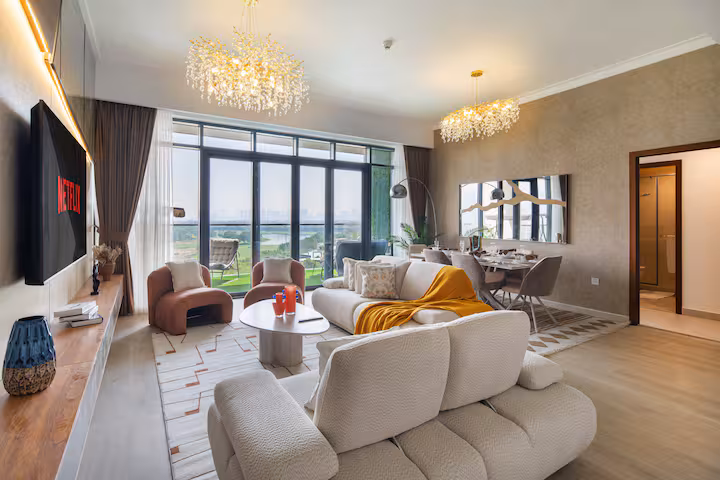 Vida Residences: The living room: a white sofa, a chandelier, tall windows onto the green
